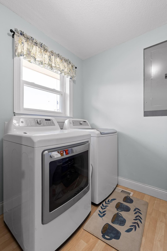 laundry room featuring light wood-type flooring, washing machine and dryer, laundry area, and electric panel