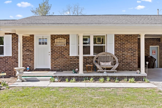 entrance to property featuring a porch, brick siding, and roof with shingles