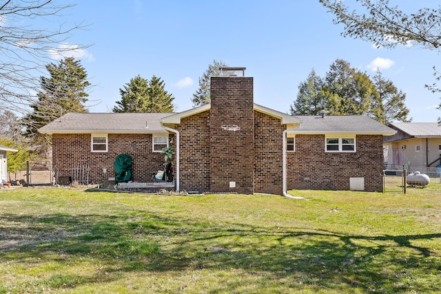 rear view of house with a yard, brick siding, a chimney, and fence