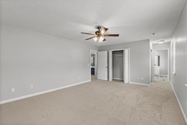 unfurnished bedroom featuring connected bathroom, ceiling fan, a textured ceiling, a closet, and light colored carpet