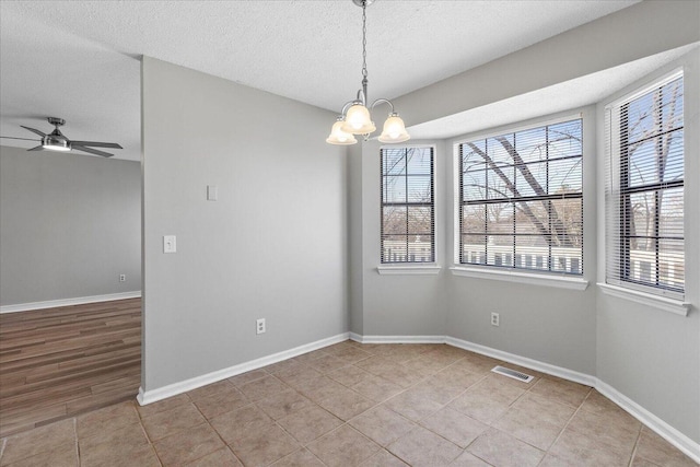 unfurnished room with a textured ceiling, light tile patterned floors, and ceiling fan with notable chandelier