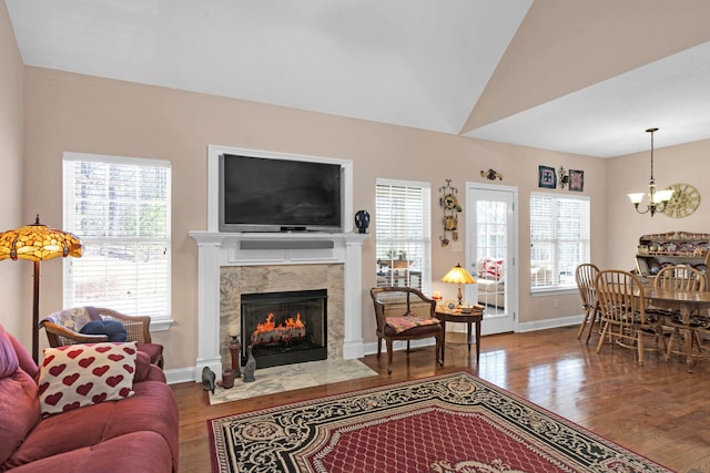 living area featuring a fireplace, a notable chandelier, lofted ceiling, wood finished floors, and baseboards