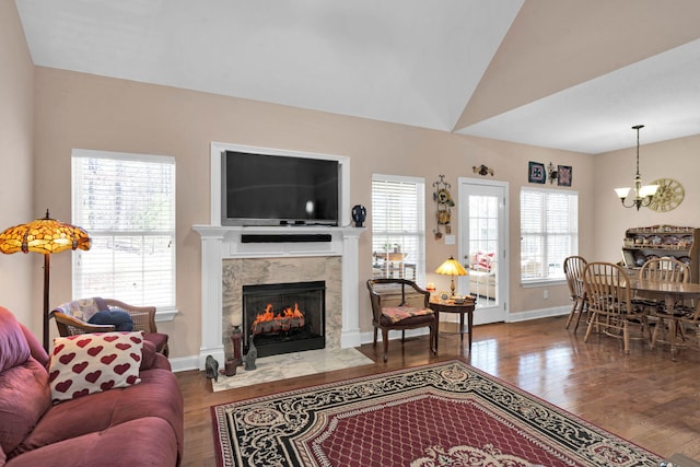 living area with baseboards, a premium fireplace, wood finished floors, vaulted ceiling, and a chandelier