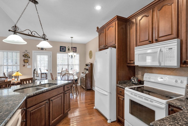 kitchen with white appliances, dark stone countertops, decorative light fixtures, a sink, and backsplash