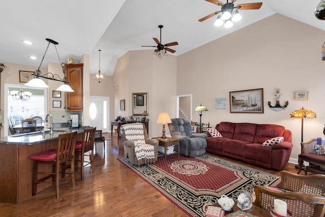 living room featuring high vaulted ceiling, wood finished floors, and ceiling fan with notable chandelier