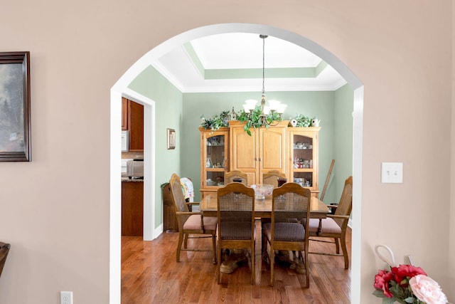 dining area with a chandelier, a raised ceiling, light wood-style flooring, and crown molding