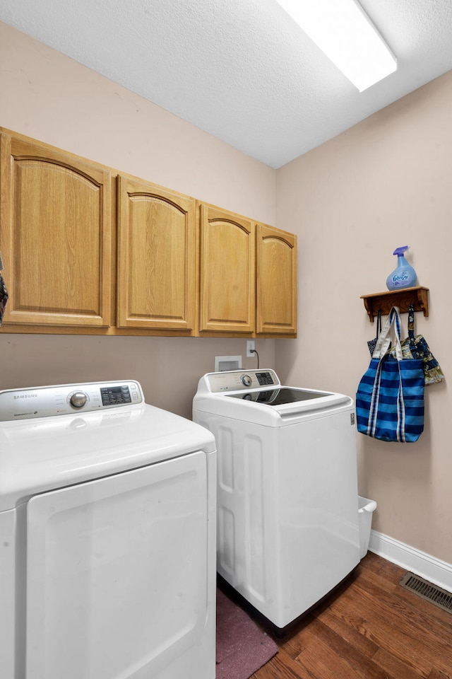 washroom featuring visible vents, baseboards, cabinet space, washer and clothes dryer, and dark wood finished floors