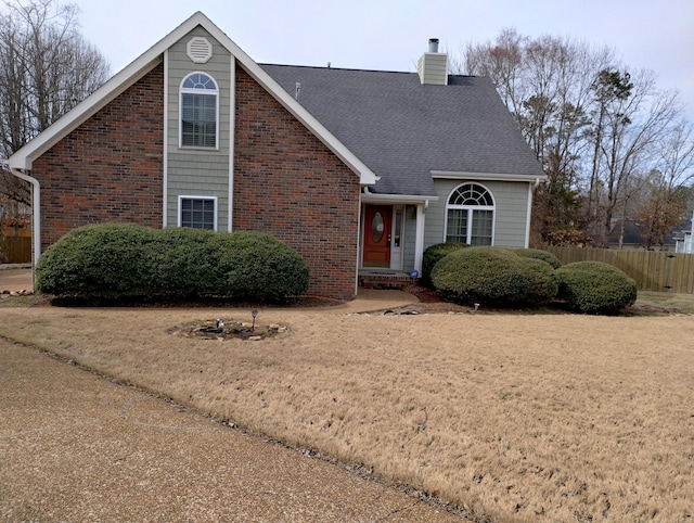 traditional-style house with brick siding, a chimney, a shingled roof, fence, and a front lawn