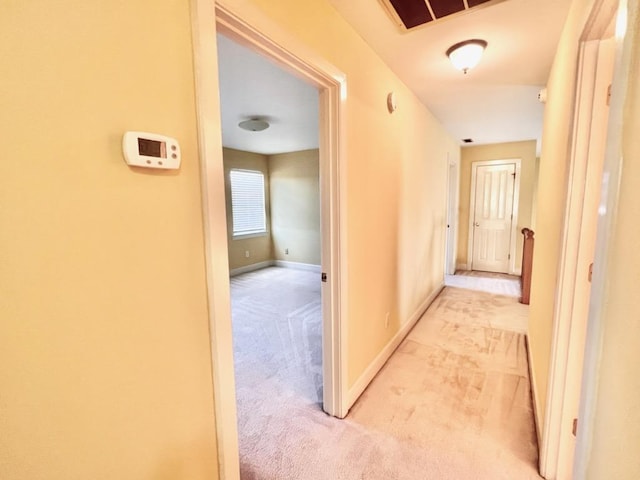 hallway with light carpet, visible vents, and baseboards