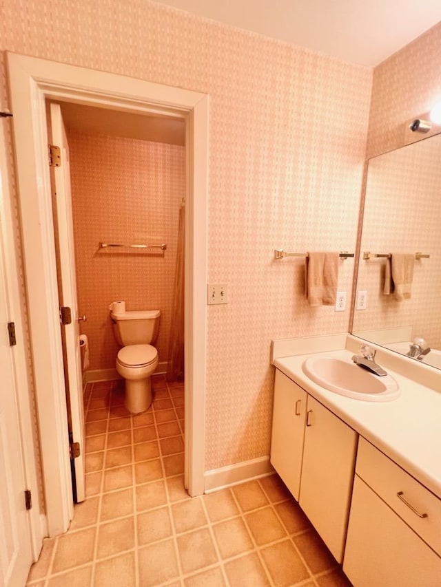 bathroom featuring tile patterned flooring, toilet, vanity, baseboards, and wallpapered walls