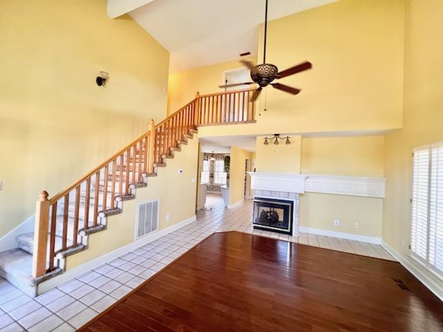 unfurnished living room featuring light tile patterned floors, high vaulted ceiling, a tile fireplace, visible vents, and stairway