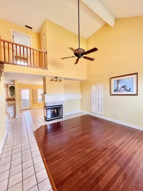 unfurnished living room with baseboards, a ceiling fan, beamed ceiling, and a multi sided fireplace