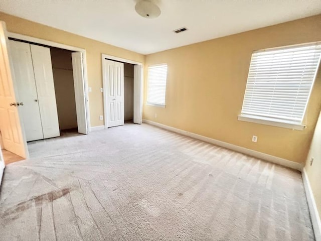 unfurnished bedroom featuring light colored carpet, two closets, visible vents, and baseboards