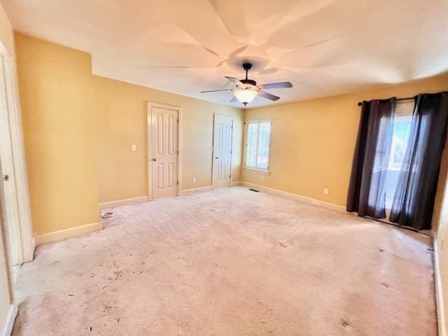 empty room featuring light carpet, a ceiling fan, and baseboards