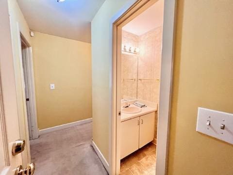 corridor with light carpet, a sink, and baseboards