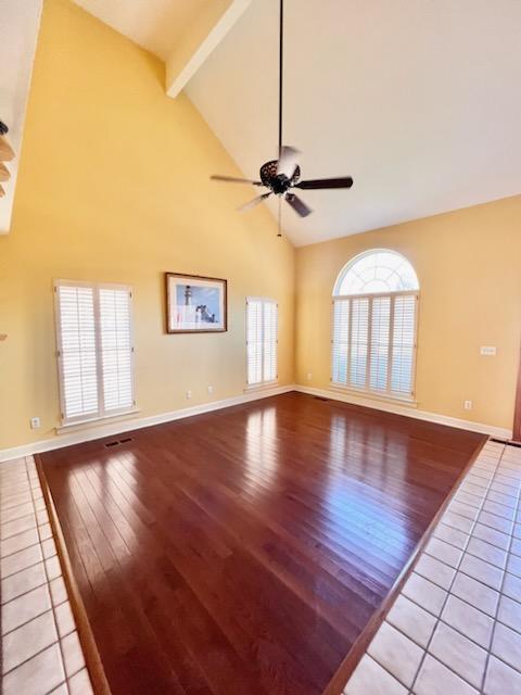 unfurnished living room featuring beam ceiling, a ceiling fan, high vaulted ceiling, light wood-type flooring, and baseboards
