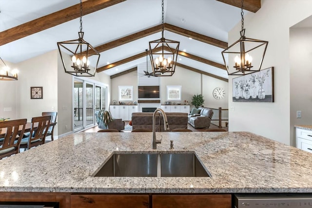 kitchen featuring a center island with sink, decorative light fixtures, sink, and light stone counters