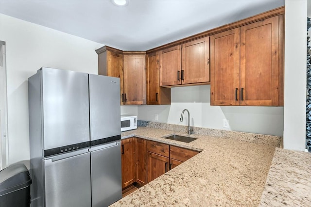 kitchen featuring sink, stainless steel refrigerator, and light stone countertops