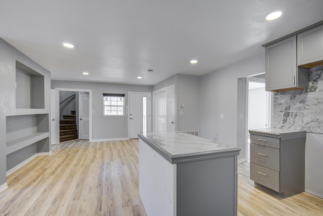 kitchen featuring a center island, light hardwood / wood-style flooring, backsplash, gray cabinets, and light stone counters