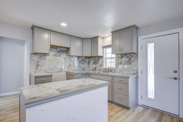 kitchen featuring a center island, gray cabinetry, light hardwood / wood-style floors, light stone countertops, and tasteful backsplash