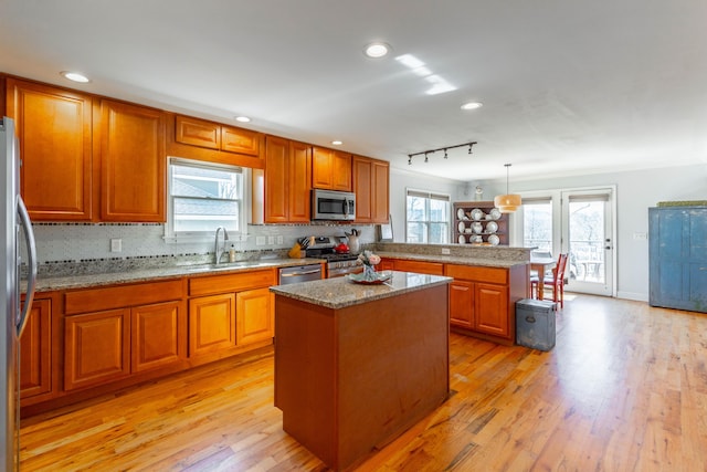 kitchen with brown cabinets, a sink, light wood-style floors, appliances with stainless steel finishes, and a peninsula