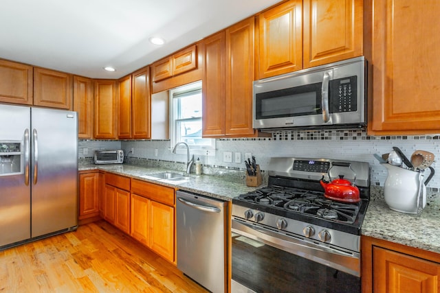 kitchen with a sink, backsplash, light wood-style floors, appliances with stainless steel finishes, and light stone countertops