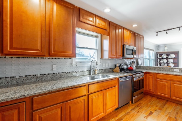 kitchen with backsplash, light stone counters, brown cabinetry, stainless steel appliances, and a sink