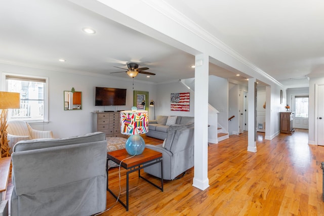 living room featuring stairs, light wood-style flooring, a ceiling fan, and ornamental molding