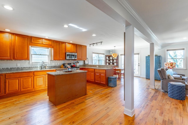 kitchen featuring stainless steel microwave, crown molding, open floor plan, a peninsula, and a sink