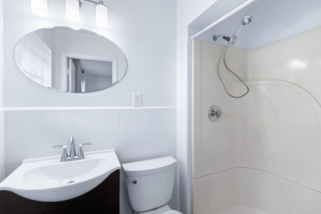 bathroom featuring tile walls, toilet, a stall shower, wainscoting, and vanity