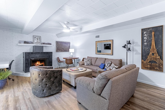 living room with wood finished floors, visible vents, baseboards, a brick fireplace, and beamed ceiling