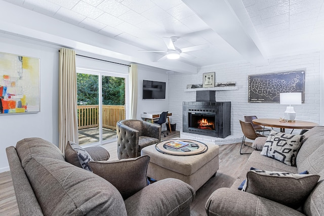 living area with brick wall, ceiling fan, wood finished floors, a fireplace, and beam ceiling