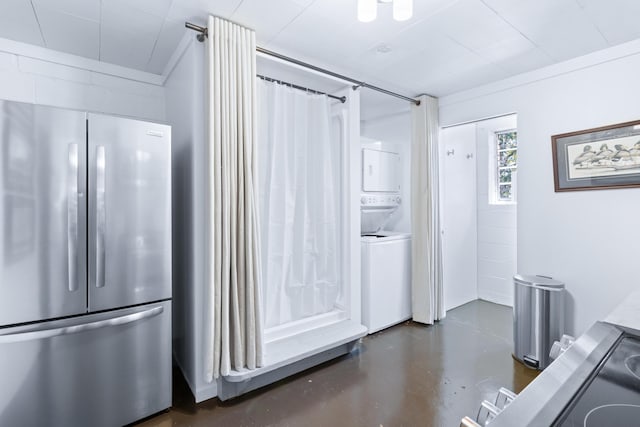 kitchen with concrete flooring, light countertops, stacked washer and clothes dryer, and freestanding refrigerator