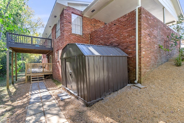 view of property exterior featuring brick siding, a shed, a deck, and an outdoor structure