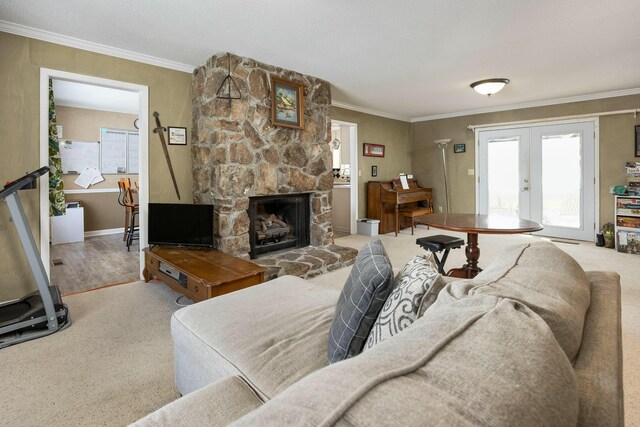 carpeted living area with crown molding, a stone fireplace, and french doors