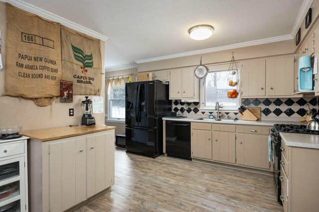 kitchen featuring black appliances, ornamental molding, light countertops, and a sink