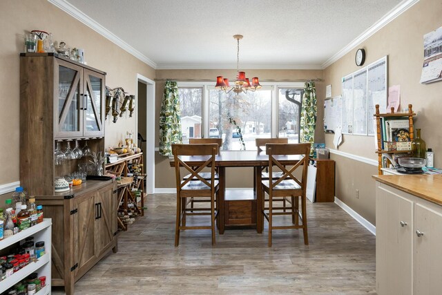 dining area with baseboards, a notable chandelier, ornamental molding, and wood finished floors