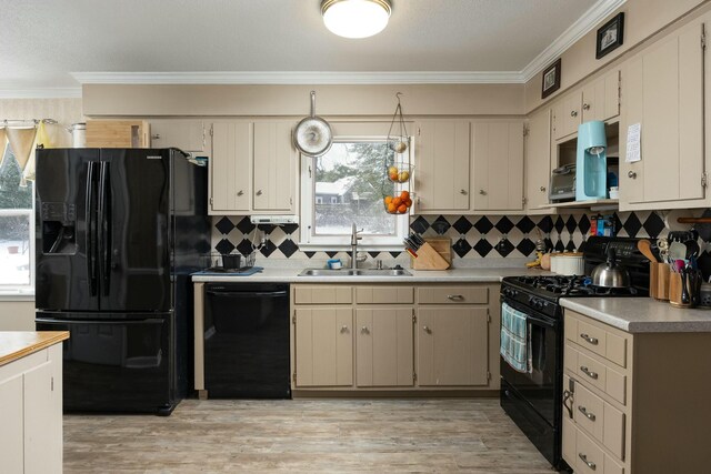 kitchen featuring crown molding, light wood finished floors, light countertops, a sink, and black appliances