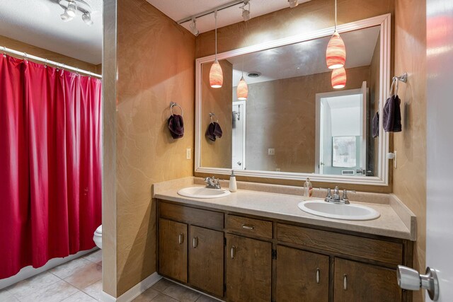 full bath featuring toilet, double vanity, a sink, and tile patterned floors