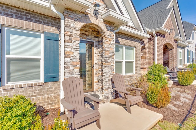 entrance to property with brick siding, a patio, and roof with shingles