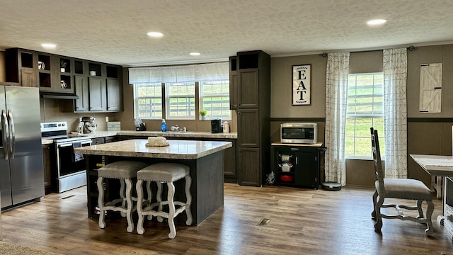 kitchen with wood finished floors, a center island, light countertops, a textured ceiling, and stainless steel appliances