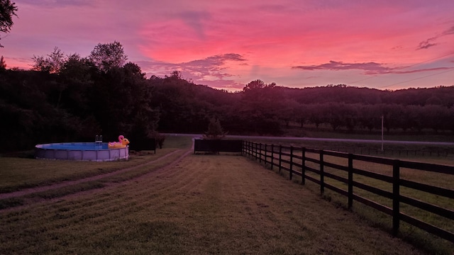 yard at dusk with a fenced in pool, a rural view, and fence