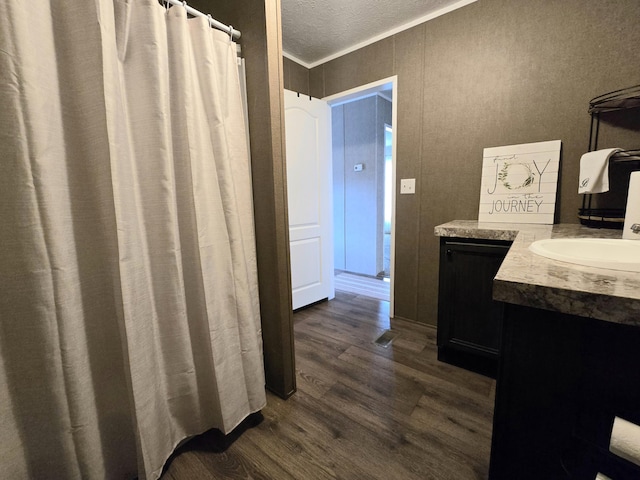 bathroom with a textured ceiling, wood finished floors, vanity, and crown molding