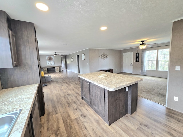 kitchen featuring light countertops, open floor plan, dark brown cabinetry, a sink, and light wood-type flooring