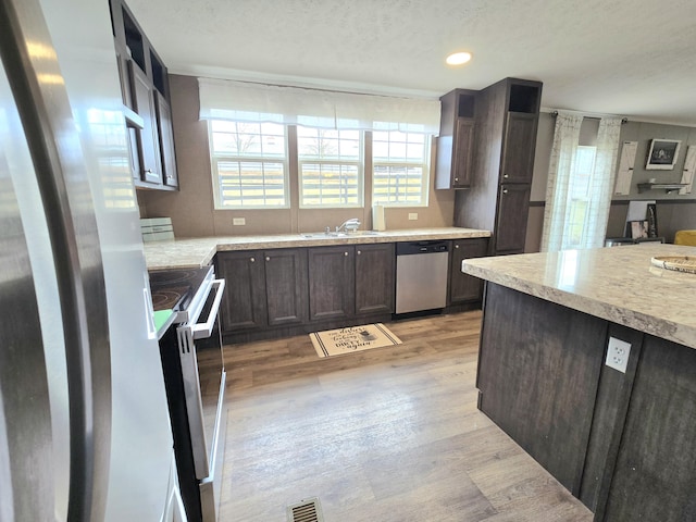 kitchen with light wood finished floors, stainless steel appliances, light countertops, visible vents, and a sink