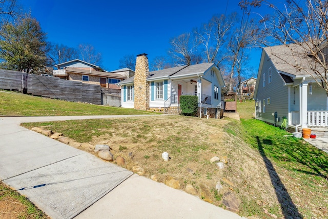 view of front facade featuring a porch, fence, a ceiling fan, a front lawn, and a chimney