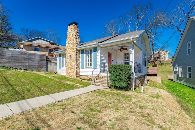 view of front of home with a porch, fence, a ceiling fan, a chimney, and a front yard