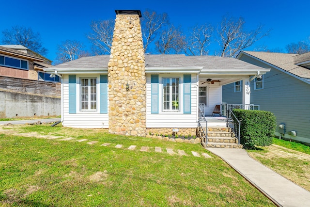 view of front of property with a chimney, a shingled roof, covered porch, a ceiling fan, and a front lawn