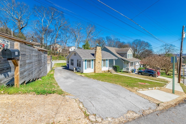 view of front of property with aphalt driveway, a chimney, a front yard, and fence