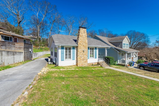 view of front of home with aphalt driveway, a chimney, a shingled roof, a front yard, and central AC